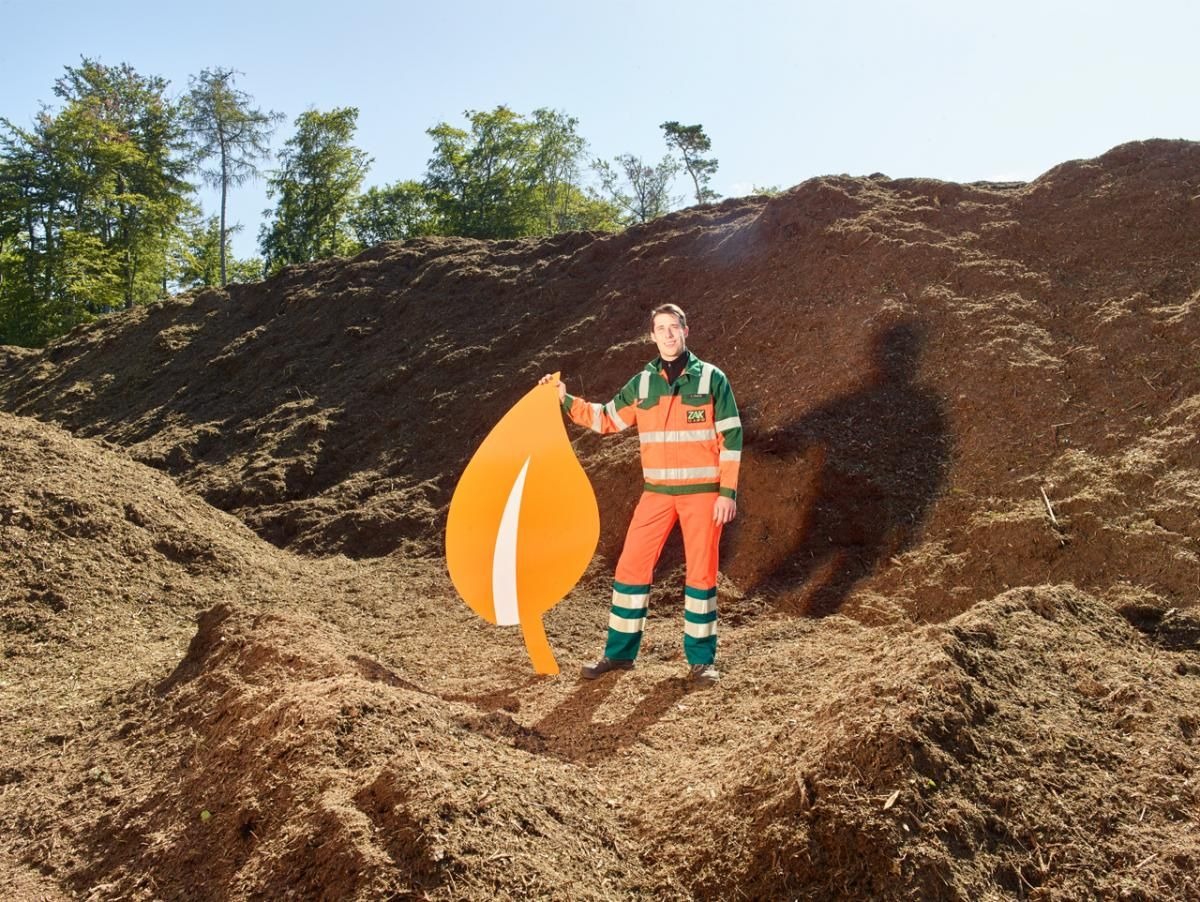 ZAK Kompost-Experte in orange Arbeitsschutzkleidung präsentiert fertig kompostierten Bioabfall zu hochwertigem PALATIHUM-Qualitätskompost