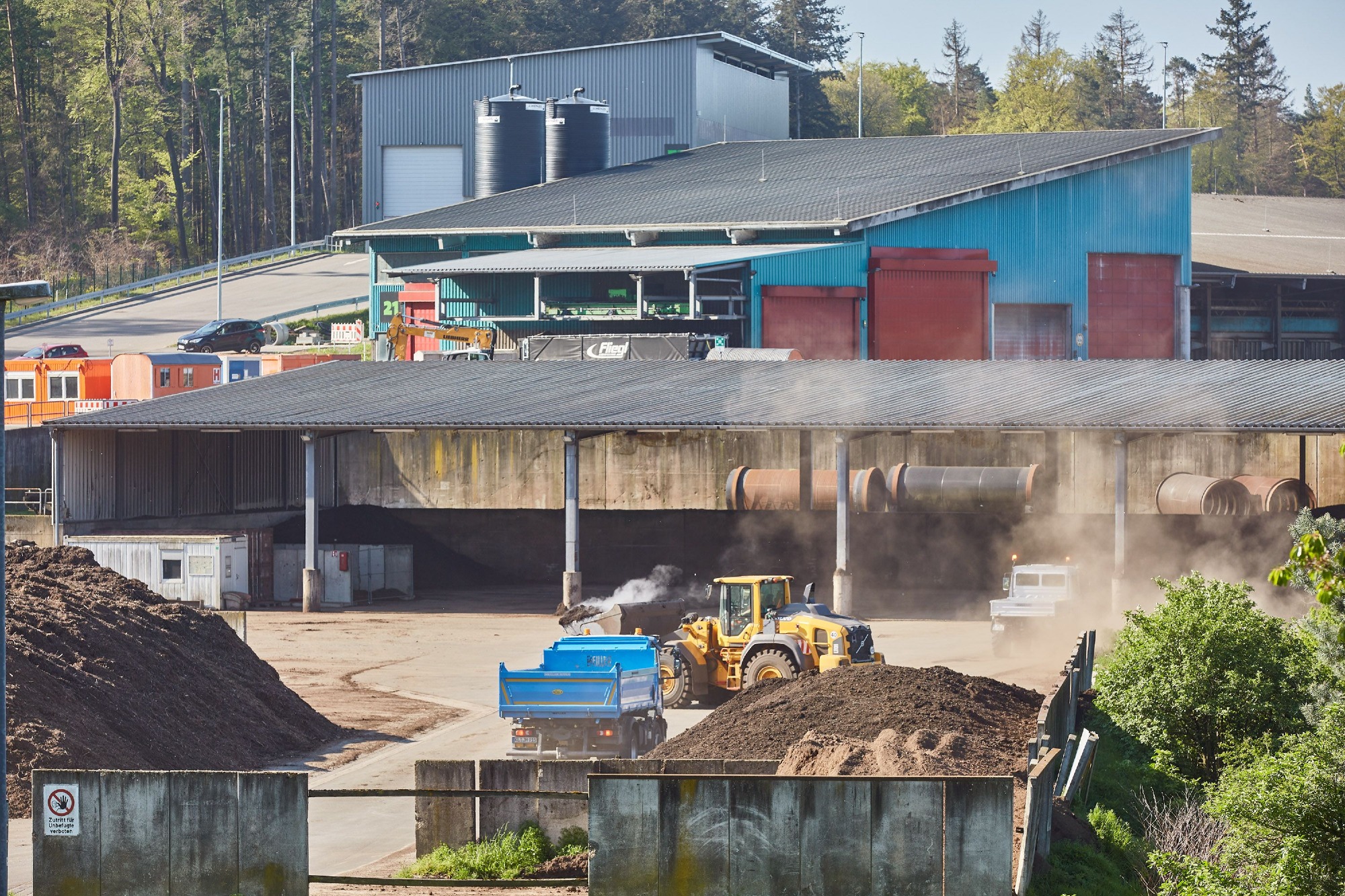 Mehrstöckige Kompostierungsanlage der ZAK verarbeitet organische Abfälle während Radlader das Material für die Weiterbehandlung bewegt