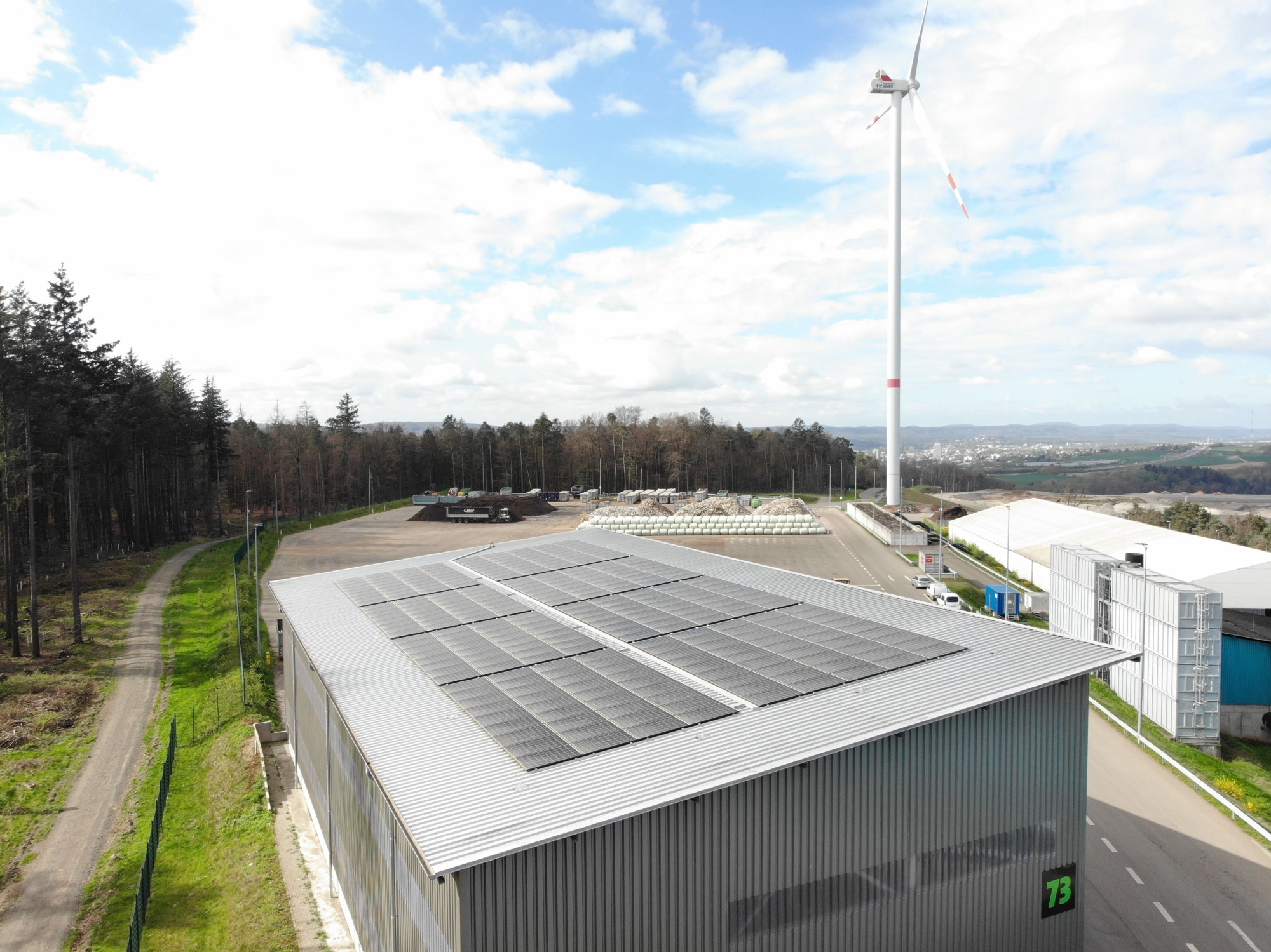 ZAK Energiedepothalle mit Solardach und Windrad in waldiger Umgebung