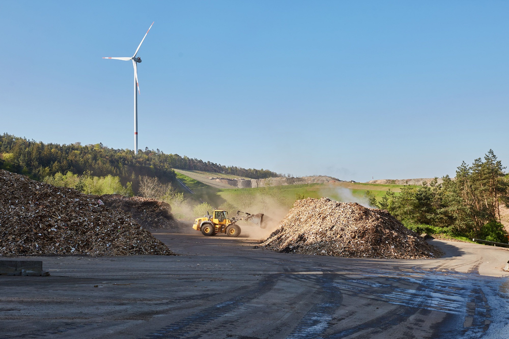 ZAK Altholzlager mit Radlader und Windkraftanlage zeigt nachhaltige Energiegewinnung aus erneuerbaren Quellen