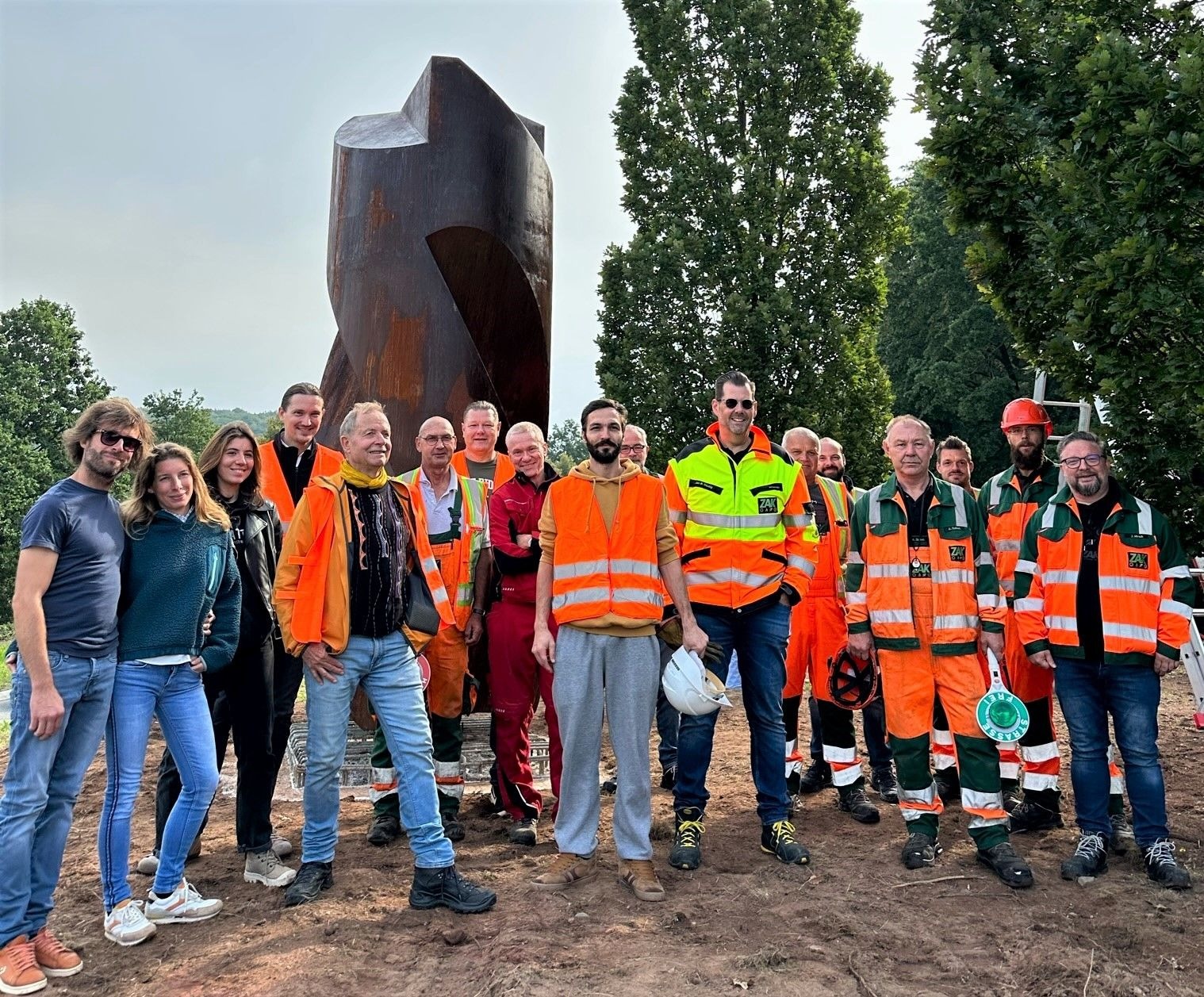ZAK-Mitarbeiter in Arbeitsschutzkleidung bei der gemeinsamen Aufstellung der Kunstskulptur "Reverse Rotation" als Lückenschluss und Verbindungselement im Verkehrskreisel vor dem östlichen Stadteingang