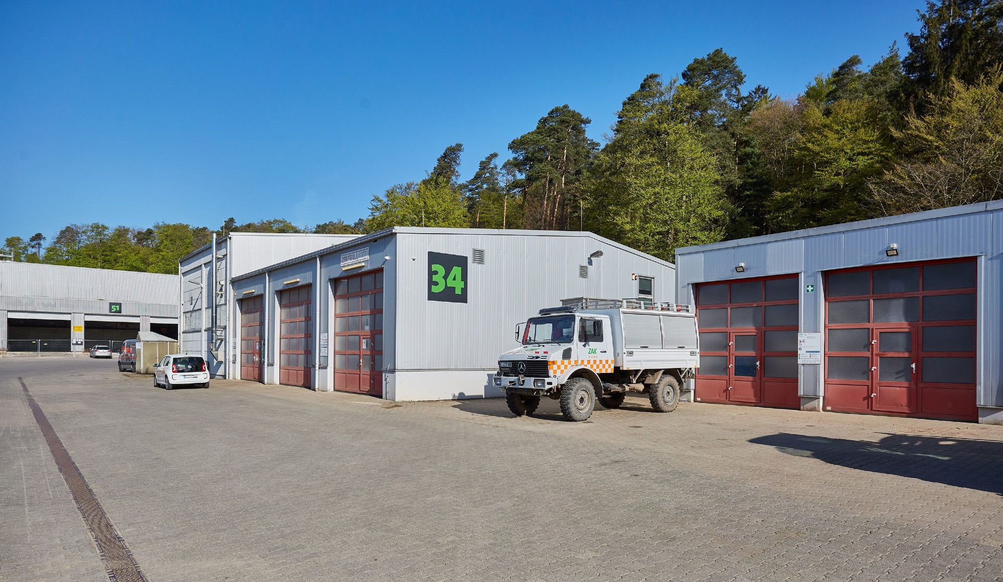 ZAK Werkstattgebäude mit Fahrzeug vor bewaldeter Kulisse