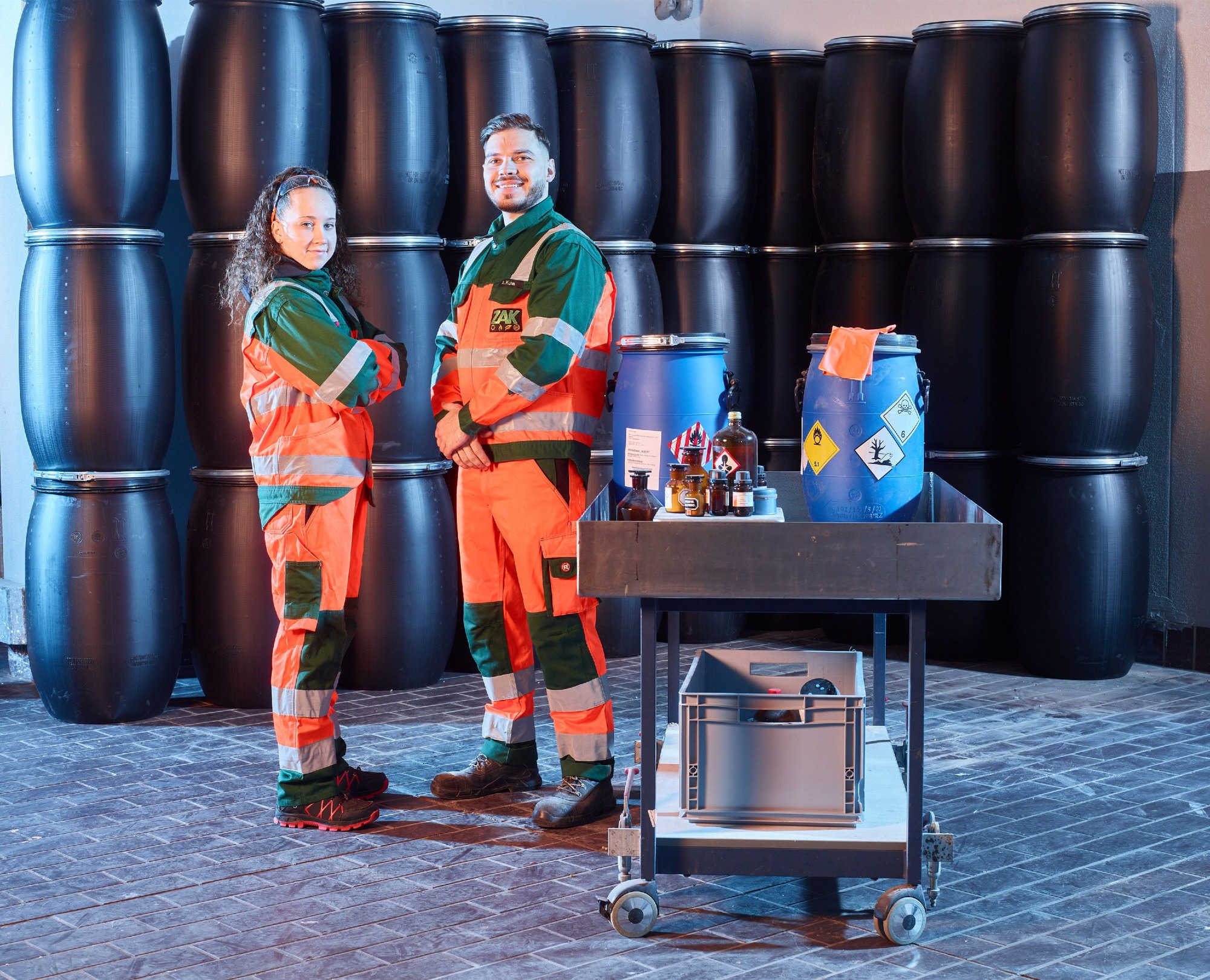 ZAK Auszubildende zur Fachkraft für Kreislauf- und Abfallwirtschaft in orangefarbener Schutzausrüstung bei praktischer Ausbildung im sicheren Umgang mit gefährlichen Abfällen