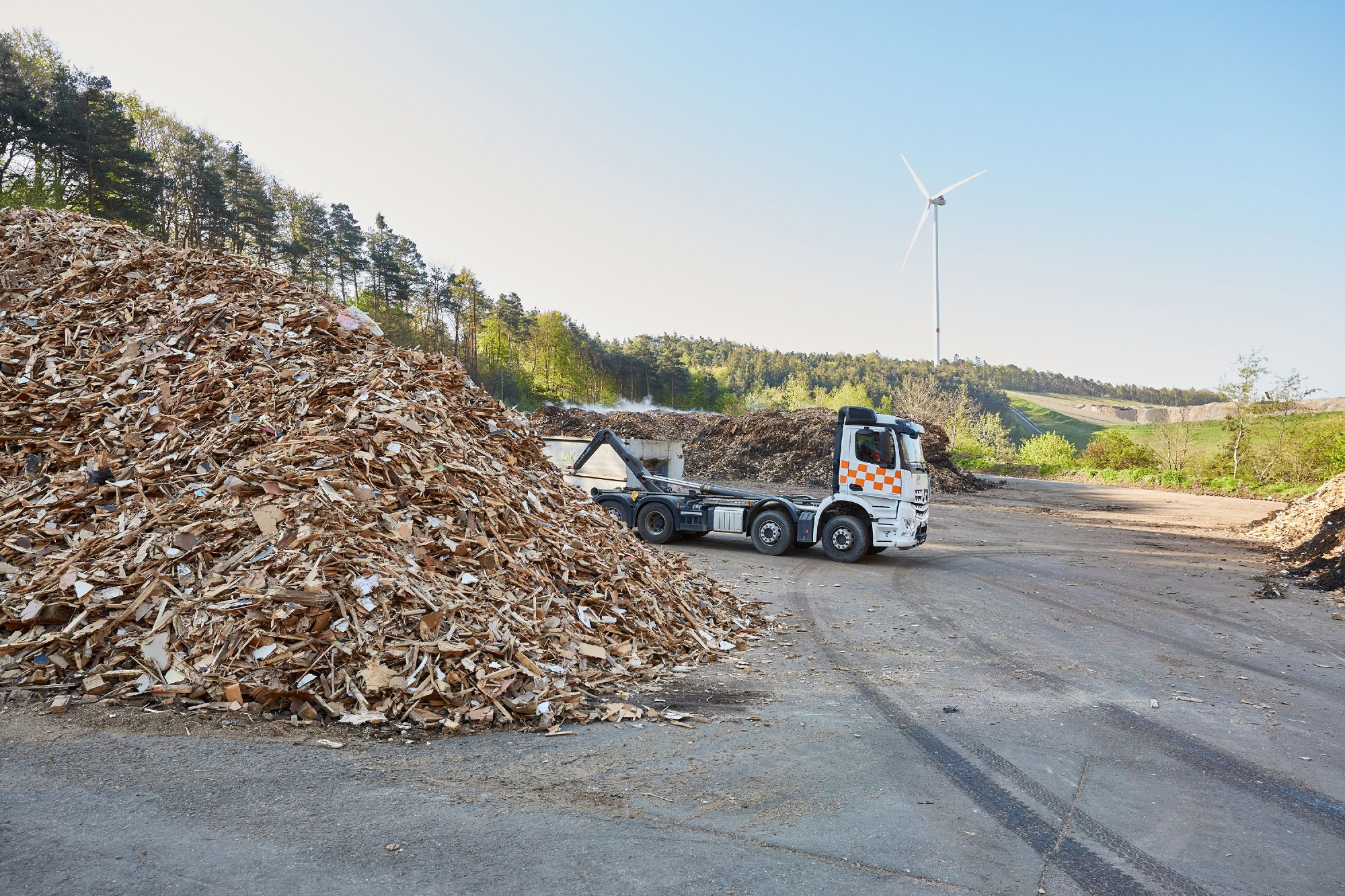 Altholzaufbereitung bei der ZAK mit großem Holzhaufen und LKW zur Weiterverarbeitung zu Biomasse-Brennstoff