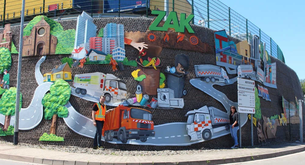 Großflächiges ZAK Kunstwerk "Garbonenwand" mit bunten Darstellungen von Müllfahrzeugen, Recyclingprozessen, Natur und Stadt als kreative Visualisierung der modernen Abfallwirtschaft