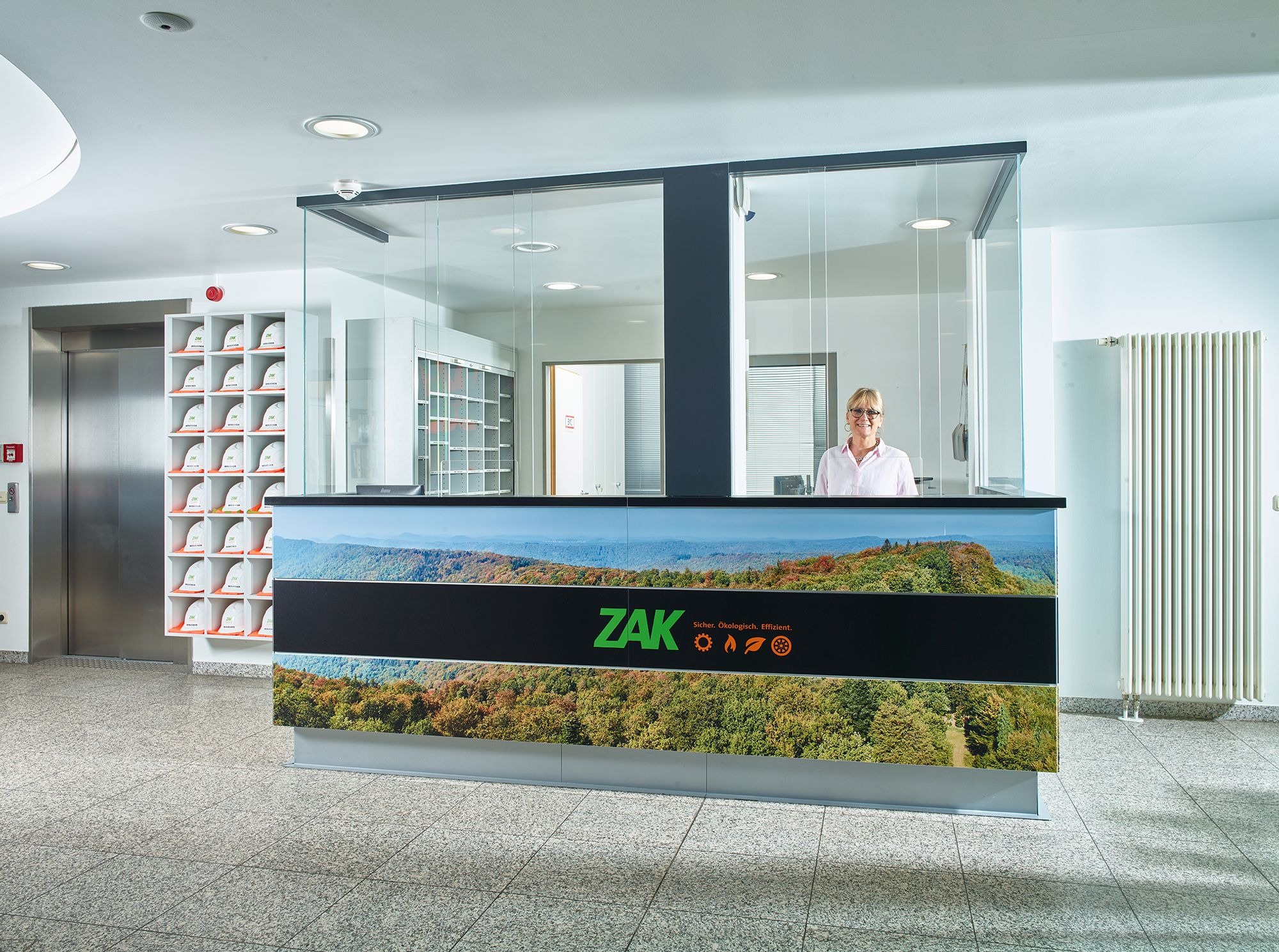 Repräsentativer Eingangsbereich der ZAK mit stilvoller Empfangstheke, Landschaftsgrafik und freundlicher Mitarbeiterbetreuung