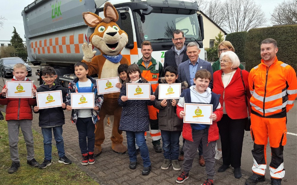 ZAK Verkehrssicherheitsinitiative "Blicki blickt's" mit Grundschulkindern, Maskottchen und Müllfahrzeug zur LKW-Gefahrenaufklärung