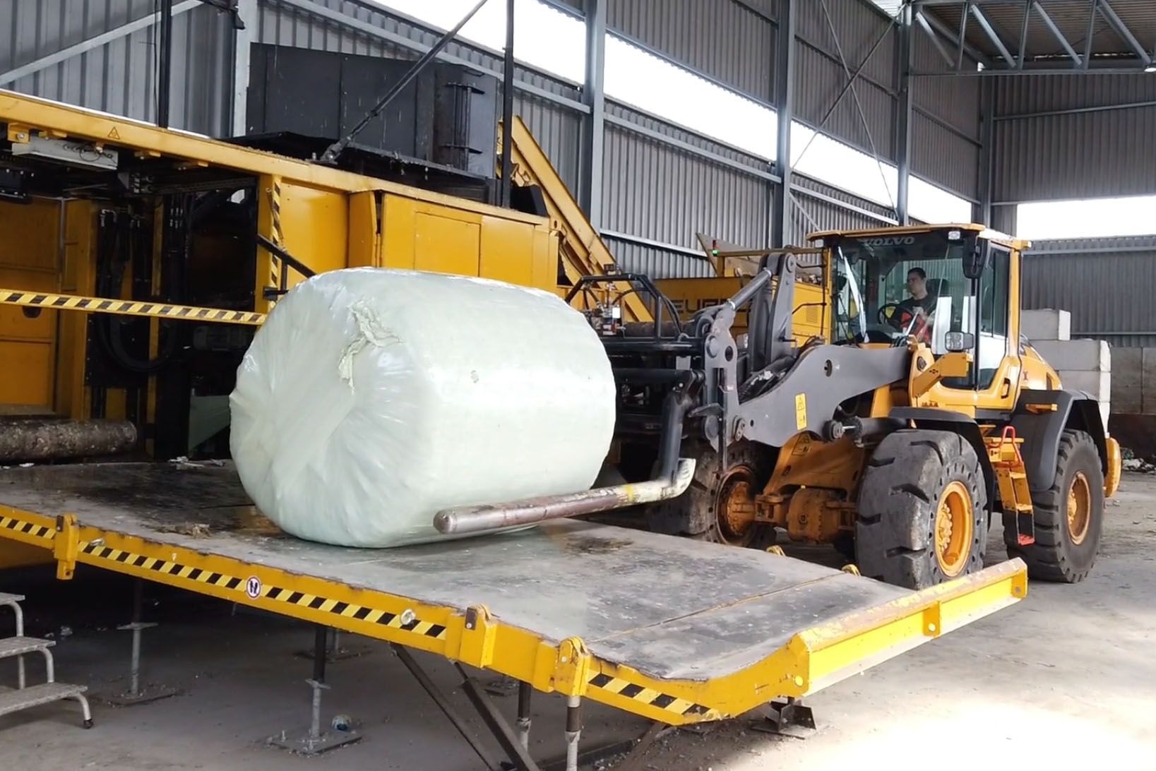 ZAK Energiedepot mit gelben Arbeitsmaschinen beim Umschlag von Silage-Rundballen für die Biomasse-Energieerzeugung